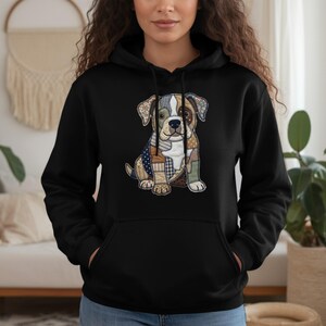 Puede incluir: Sudadera con capucha negra con un diseño de perro patchwork. La ilustración del perro presenta una mezcla de telas estampadas en tonos azules, marrones y blancos. La sudadera tiene un bolsillo de canguro y una capucha con cordón.