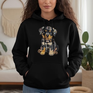 May include: Black hoodie featuring a colorful patchwork dog graphic. The dog design incorporates plaid, floral, and leopard print patterns. The hoodie has a drawstring hood and a front kangaroo pocket, offering a casual and comfortable style.