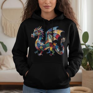 Puede incluir: Sudadera con capucha negra con un diseño de dragón colorido. El dragón presenta un patrón de retazos en tonos azules, rojos, amarillos y verdes. La sudadera tiene un bolsillo de canguro y una capucha con cordón.