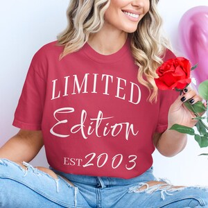 Könnte beinhalten: Ein rotes T-Shirt mit weißem Text, der "LIMITED EDITION EST 2003" lautet. Die Person, die das Shirt trägt, hält eine rote Rose.