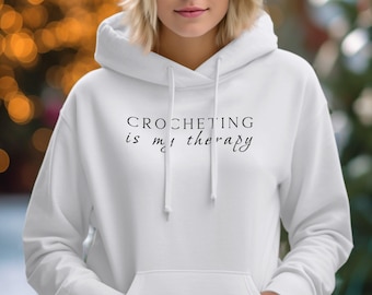 May include: White hoodie with the text "CROCHETING is my therapy" printed in black.