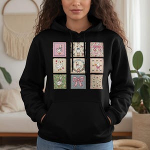 May include: Black hooded sweatshirt featuring nine square patches with goose and bow designs. The patches have various patterns, including gingham, polka dots, and floral prints. Some patches include the text "Coquette" and "My Goose Club".