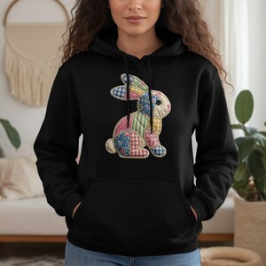May include: Black hoodie featuring a colorful patchwork bunny design. The bunny is made of various patterned fabrics in shades of blue, pink, yellow, and green. The hoodie has a front pocket and a drawstring hood.