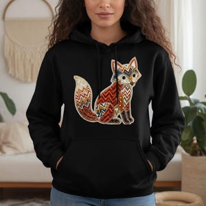 May include: Black hoodie with a detailed fox illustration. The fox design incorporates patterns in red, orange, blue, and white. The hoodie includes a kangaroo pocket and a drawstring hood. The fox image is positioned centrally on the front of the garment.
