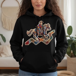 Puede incluir: Sudadera con capucha negra con un gráfico colorido de una persona montando a caballo. El gráfico tiene un diseño de patchwork con detalles en rojo, azul y amarillo. El caballo y el jinete están sobre un patrón en zigzag.
