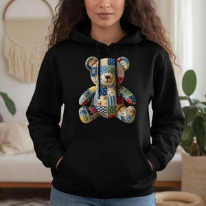 Pode incluir: Moletom preto com um design colorido de urso de pelúcia em patchwork. O urso tem uma variedade de tecidos estampados em tons de azul, vermelho, amarelo e verde. O moletom tem um bolso frontal e um capuz com cordão.