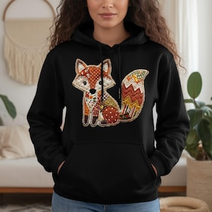 May include: Black hoodie with a colourful fox appliqué. The fox design features polka dots, floral prints, and geometric shapes in orange, brown, and green. The hoodie has a kangaroo pocket and a drawstring hood, a classic casual style.