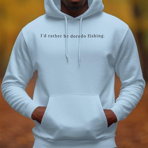 以下が含まれることがあります： 前面に「I'd rather be dorado fishing.」という文字がプリントされた薄いブルーのパーカー