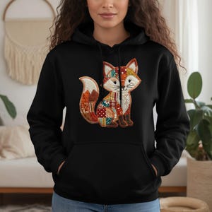May include: Black hoodie featuring a colorful fox applique. The fox design incorporates patchwork patterns in shades of red, orange, green, and brown. The hoodie has a drawstring hood and a front pocket.
