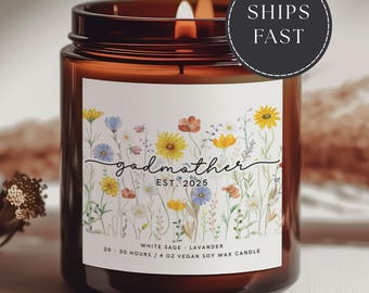 May include: A lit brown glass candle jar with a floral label. The label reads "godmother EST. 2025" and "WHITE SAGE - LAVENDER". The candle is 4 oz and made of vegan soy wax. The image also includes a "SHIPS FAST" sticker.
