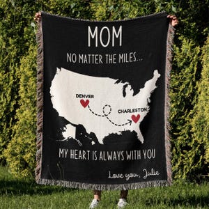 May include: Black woven throw blanket with a white outline of the United States map. The map shows a dotted line connecting Denver, Colorado to Charleston, South Carolina with red hearts marking each city. The text "MOM, NO MATTER THE MILES... MY HEART IS ALWAYS WITH YOU, Love you, Julie" is printed on the blanket.