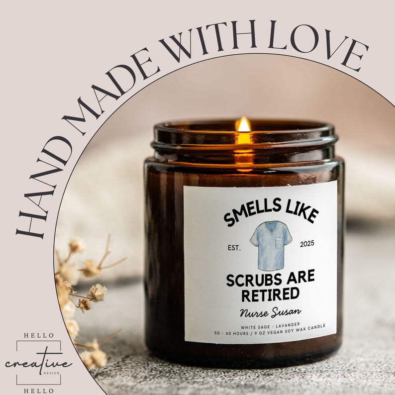 May include: A lit brown glass candle jar with a white label that reads "Smells Like Scrubs Are Retired Nurse Susan". The candle has a blue scrub top graphic and the text "Hand Made With Love".