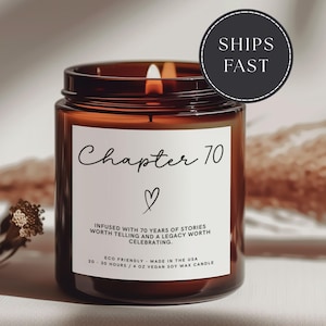 May include: A lit amber glass candle with a white label that reads "Chapter 70" with a heart symbol. The candle is infused with 70 years of stories and is made with vegan soy wax. The candle burns for 20-30 hours and is 4 oz.