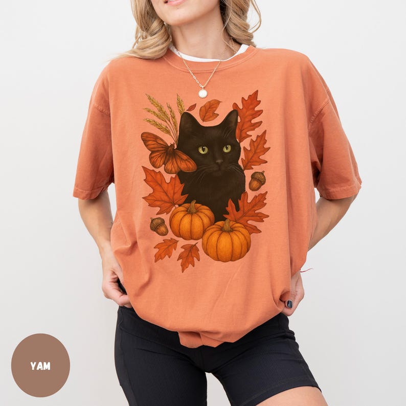 Pu&ograve; includere: T-shirt arancione con un disegno di gatto nero circondato da foglie autunnali, zucche e una farfalla. La grafica ha un tema autunnale, con colori caldi e illustrazioni dettagliate. La maglietta &egrave; uno stile casual e confortevole.