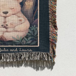 May include: A woven tapestry with a dark blue background featuring two white polar bears cuddling. The tapestry has a fringe border with colorful threads. The text "Julie and Laura" is printed at the bottom of the tapestry.