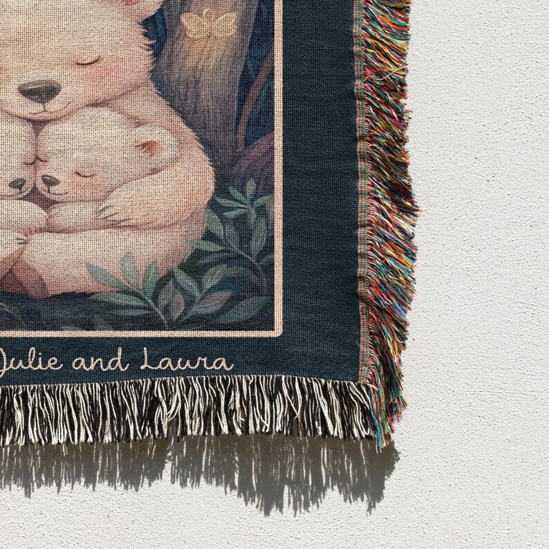 May include: A woven tapestry with a dark blue background featuring two white polar bears cuddling. The tapestry has a fringe border with colorful threads. The text "Julie and Laura" is printed at the bottom of the tapestry.