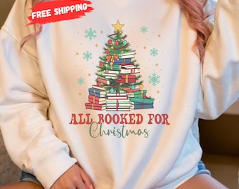 May include: White sweatshirt featuring a Christmas tree design made of books, decorated with ornaments and a star. The text "ALL BOOKED FOR Christmas" is printed below the tree. Snowflake and star graphics are also present.