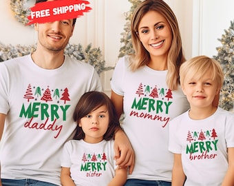 May include: Four white t-shirts with matching Christmas tree designs and the words "Merry Daddy," "Merry Mommy," "Merry Sister," and "Merry Brother" in green and red. The family is wearing blue jeans.