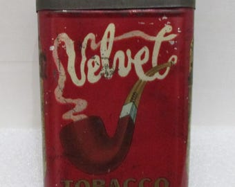 Può includere: Scatola di latta rossa con la parola "Velvet" in bianco in corsivo e la parola "Tobacco" in lettere dorate. Una pipa rossa con un bocchino bianco è raffigurata sulla scatola.