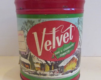Può includere: Scatola di latta rossa, verde e bianca con una scena invernale e le parole "Velvet Pipe & Cigarette Tobacco" sull'etichetta.