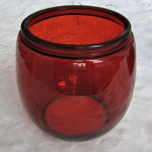 May include: A deep red glass jar with a rounded shape and a wide opening. The jar is made of thick glass and has a smooth, polished finish.