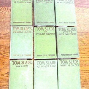 Puede incluir: Nueve libros vintage verdes de Tom Slade de Percy Keese Fitzhugh están dispuestos sobre una superficie de madera. Los títulos incluyen "At Temple Camp", "On the River" y "On Mystery Trail". Los libros son de color verde claro.