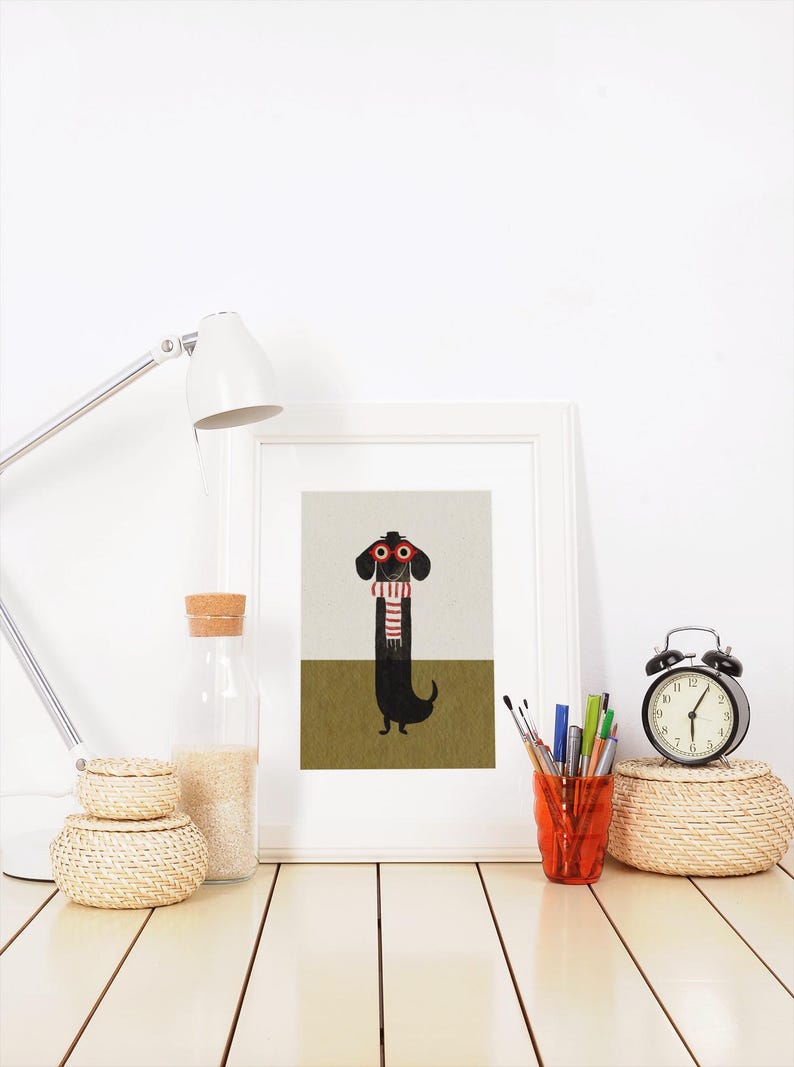 May include: A framed print of a black dachshund wearing red glasses and a red and white striped scarf. The dachshund is standing on a green background.