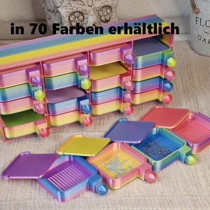Könnte beinhalten: Ein mehrfarbiger Regenbogen-Aufbewahrungsorganizer mit sechzehn kleinen Schubladen und mehreren herausnehmbaren Fächern davor. Die Einheit zeigt einen Farbverlauf in Pink, Gelb, Blau und Lila. Der Text "in 70 Farben erhältlich" ist zu sehen.