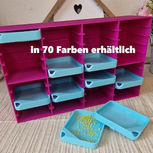 Könnte beinhalten: Ein magenta-farbener Aufbewahrungs-Organizer mit mehreren Fächern und hellblauen Tabletts. Der Text "in 70 Farben erhältlich" ist auf dem Organizer zu sehen. Zwei hellblaue Tabletts befinden sich vor dem Organizer, eines davon ist mit gelben Perlen gefüllt.
