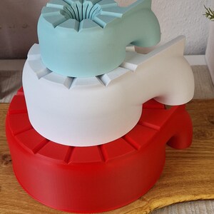 May include: Three-tiered, abstract sculptures in red, white, and light blue. Each level has a unique shape, with the top level featuring a flower-like design. The sculptures are stacked on top of each other.