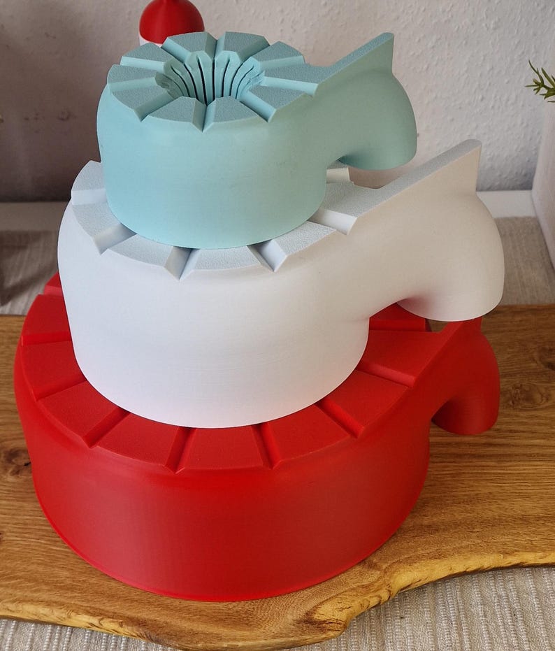 May include: Three-tiered, abstract sculptures in red, white, and light blue. Each level has a unique shape, with the top level featuring a flower-like design. The sculptures are stacked on top of each other.