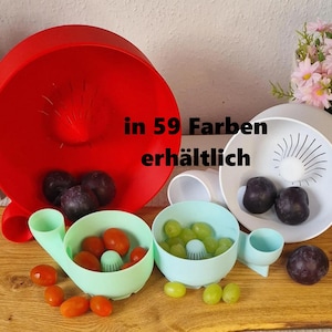 May include: A collection of colorful fruit washing bowls in red, white, and light blue, with a wooden cutting board base. The bowls contain grapes and tomatoes. The text "in 59 Farben erh&auml;ltlich" is visible.