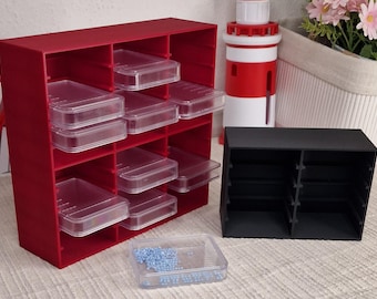 Puede incluir: Un organizador de almacenamiento rojo con múltiples compartimentos y cajones de plástico transparente. A su lado hay un organizador negro más pequeño. Un recipiente de cuentas azules está frente a los organizadores. Un objeto rojo y blanco con forma de faro en el fondo.