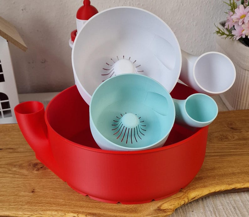 May include: A set of colorful kitchen tools, including a large red bowl with a handle, a white bowl, and a smaller teal bowl. The bowls have a unique design with drainage holes.