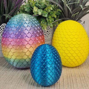 Könnte beinhalten: Drei dracheneierförmige Ornamente, eines ist regenbogenfarben schillernd, eines ist gelb und eines ist blau.