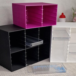 Könnte beinhalten: Drei würfelförmige Aufbewahrungsorganisatoren in Schwarz, Weiß und Magenta. Jeder Organizer hat mehrere Fächer. Klare Kunststoffschalen sind in einigen Fächern sichtbar. Die Organizer sind für die Schreibtisch- oder Bastelaufbewahrung konzipiert.