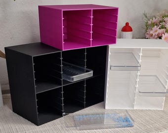 Puede incluir: Tres organizadores de almacenamiento en forma de cubo en negro, blanco y magenta. Cada organizador tiene múltiples compartimentos. Se ven bandejas de plástico transparente en algunos compartimentos. Los organizadores están diseñados para el almacenamiento de escritorio o manualidades.