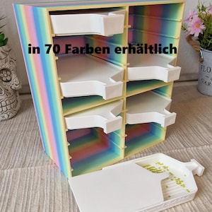 Könnte beinhalten: Ein regenbogenfarbener Aufbewahrungsorganizer mit acht Fächern für weiße Schalen, der den Text in 70 Farben erhältlich zeigt. Die Einheit ist vertikal ausgerichtet, hat ein pastellfarbenes Farbverlauf-Finish und eine weiße Schale davor.