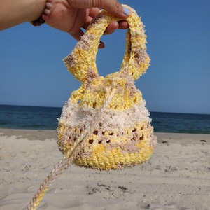 May include: A crocheted bag with a yellow, white, and brown striped pattern. The bag has a drawstring closure and a long handle.
