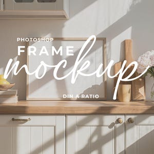 Può includere: Una scena di cucina con un piano di lavoro in legno e mobili bianchi. Sul bancone ci sono un mockup incorniciato, taglieri, una tazza e un vaso di fiori. Il testo "Photoshop Frame Mockup" è sovrapposto.