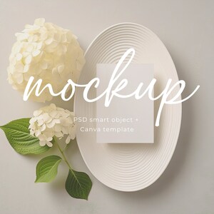 May include: White card mockup on a white plate with white hydrangeas. The text "mockup" is written in white script on the image. The text "PSD smart object + Canva template" is written in black below the card.