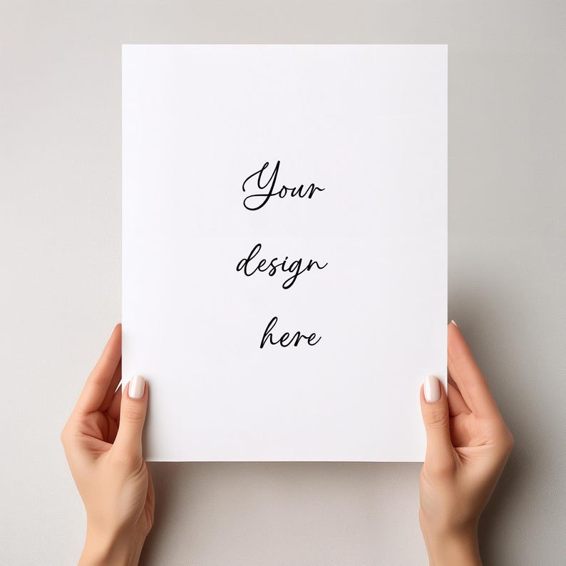 May include: A white rectangular paper held by two hands, with the words "Your design here" written in elegant cursive script. The paper is centered and the background is a solid light gray.