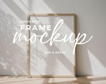 May include: A rectangular wooden frame mockup with a white mount, leaning against a light-coloured wall. The text "Photoshop Frame Mockup DIN A Ratio" is overlaid in white script. Natural light and shadows are cast on the wall.