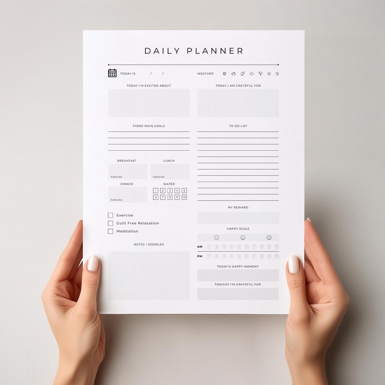 May include: A white daily planner with black text, held by hands. The planner includes sections for goals, to-do lists, and tracking habits. The text "DAILY PLANNER" is at the top. Sections include "Today I'm Excited About" and "Today I Am Grateful For."