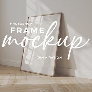 May include: A rectangular wooden frame mockup leaning against a white wall on a light wood floor. The frame is empty, with the text "Photoshop Frame Mockup" in white script. The scene is lit by natural light.