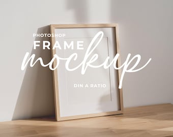 May include: A wooden frame mockup with a white mount, leaning against a white wall. The frame is on a wooden surface. The text "Photoshop Frame Mockup DIN A Ratio" is overlaid on the image.