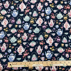 May include: Dark navy fabric with a repeating pattern of teapots, teacups, and floral arrangements in pink, blue, and yellow. The fabric has a ruler along the bottom edge. The text "DOKTIMA TEA GARDEN" is visible.