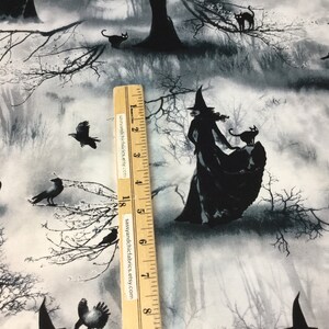 May include: Black and white Halloween-themed fabric featuring silhouettes of witches, black cats, and crows in a misty forest setting. The fabric has a grayscale color palette with a ruler for scale.