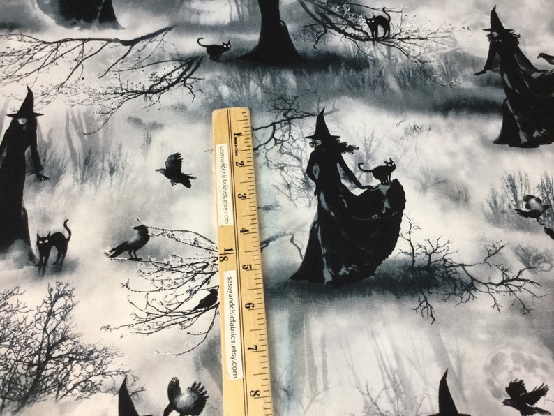 May include: Black and white Halloween-themed fabric featuring silhouettes of witches, black cats, and crows in a misty forest setting. The fabric has a grayscale color palette with a ruler for scale.