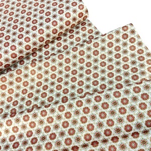 May include: Fabric with a repeating floral pattern in shades of red, gray, and gold on a cream background. The fabric is folded and rolled, showcasing the detailed design. Ideal for sewing and crafting projects.